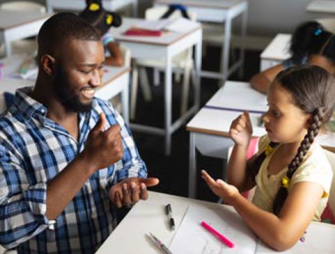 Children sitting at a table with an adult using sign language