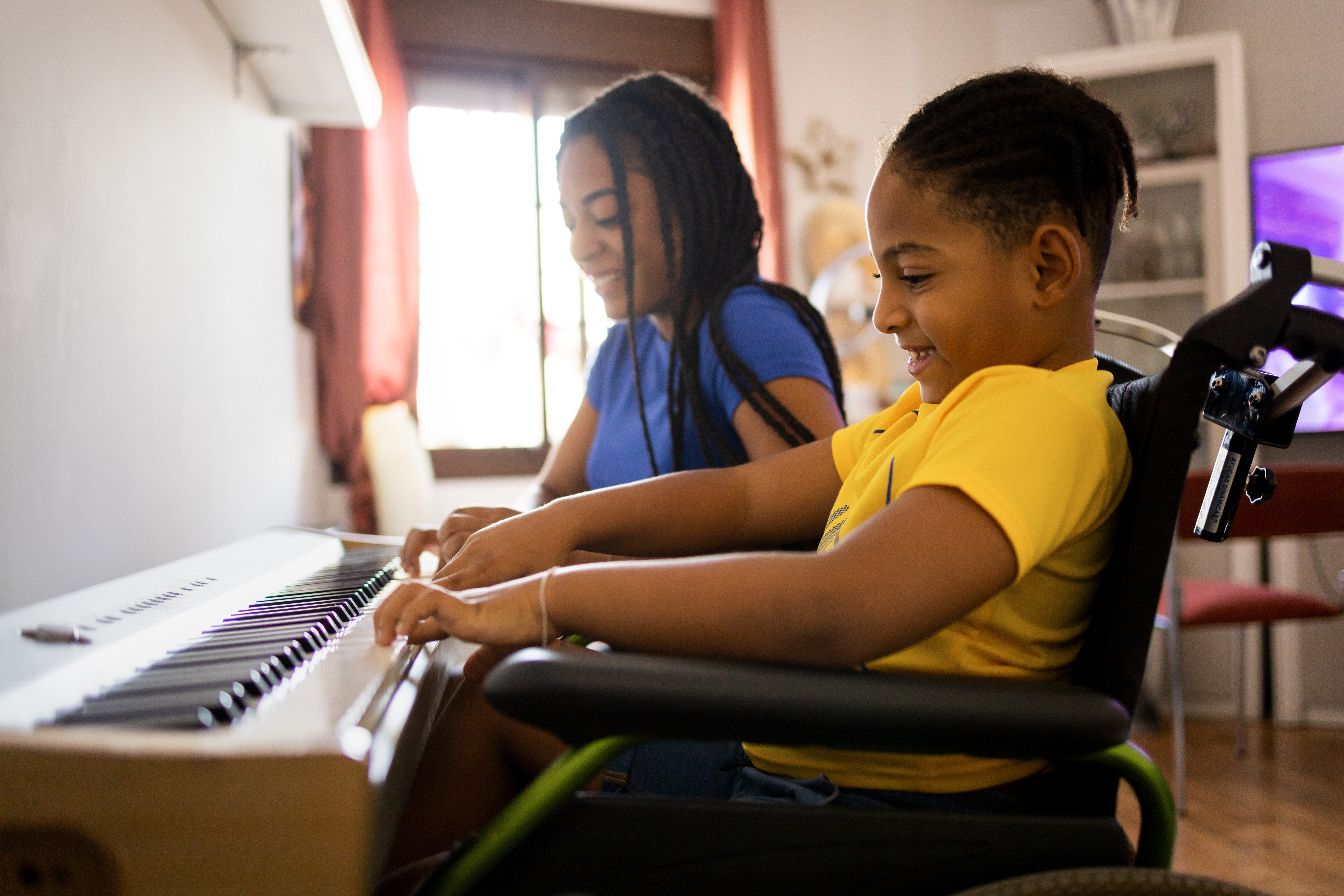 Young boy in wheelchair playing piano with someone else also at the piano.